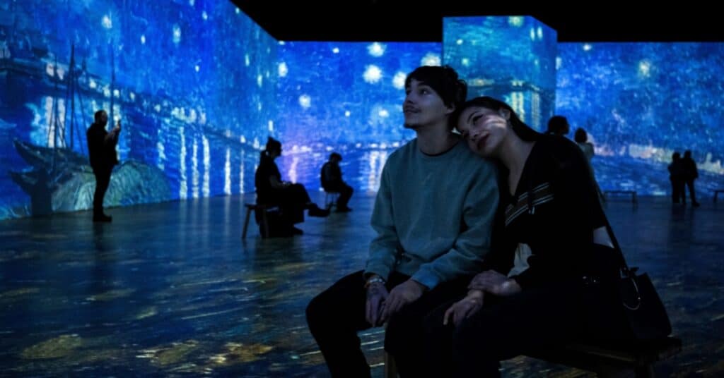 A couple sitting on a bench surrounded by projections of Van Gogh's Starry Night